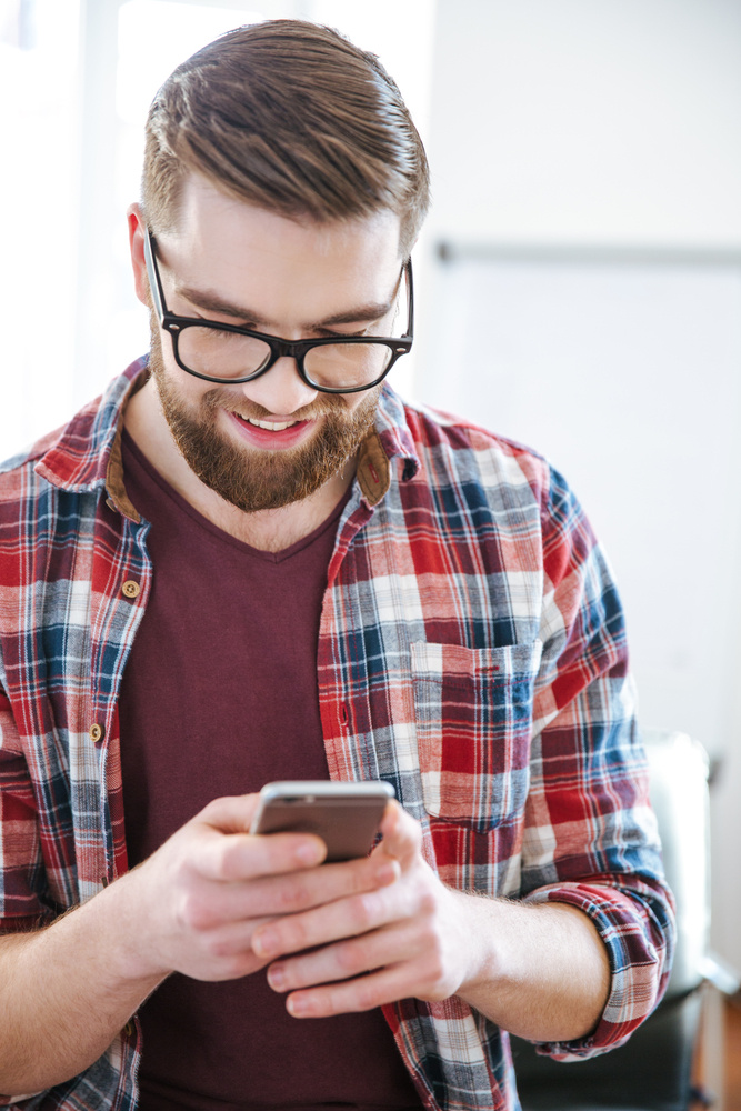Closeup of smiling handsome bearded man in checkered shirt using mobile phone